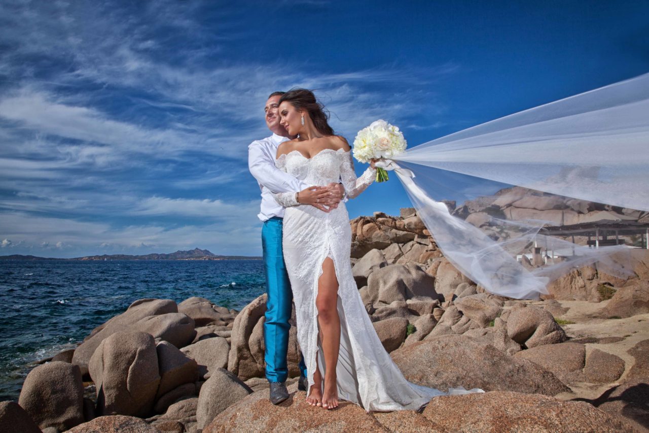 Sposi abbracciati sugli scogli in riva al mare. Foto scattata da Giuseppe Ortu fotografo specializzato in matrimoni a Olbia.